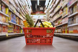 Red shopping basket filled with fresh fruits and vegetables in grocery store aisle.