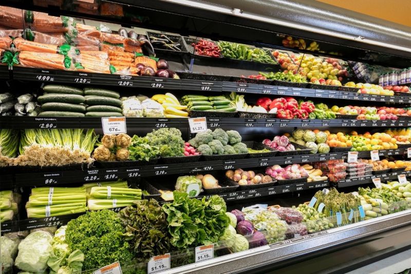 Grocery store produce aisle stocked with fresh vegetables and fruits.