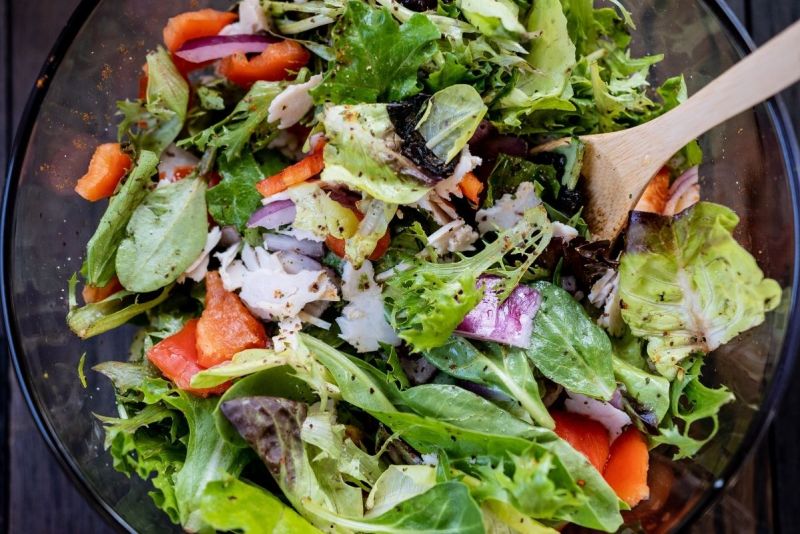 Fresh mixed salad with leafy greens, tomatoes, and onions in a glass bowl.