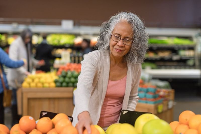 Woman shopping for fresh oranges at a grocery store produce section.