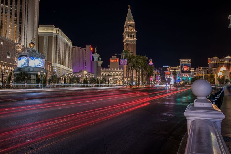 Long-exposure night photo of the Las Vegas Strip with colorful light trails and major resorts glowing.