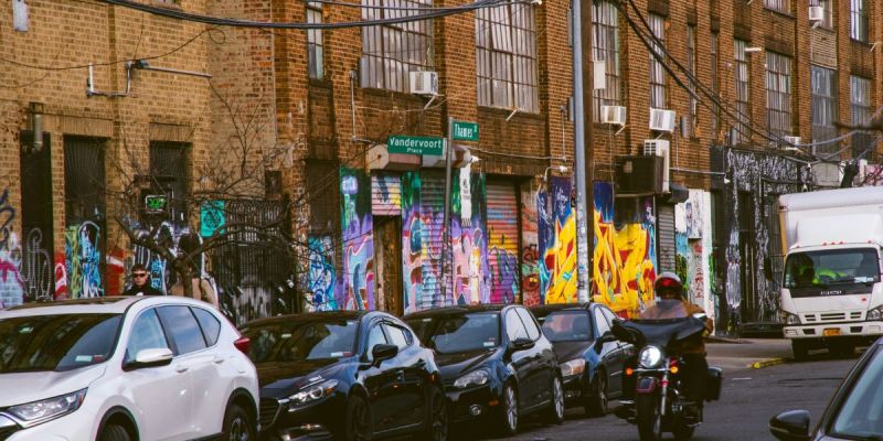 Bushwick Brooklyn street with colorful murals, parked cars, and urban scenery