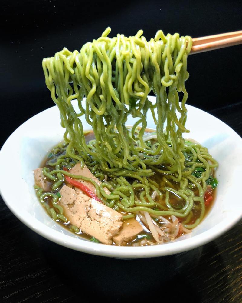 Bowl of vegan green ramen noodles lifted with chopsticks at a Las Vegas restaurant.