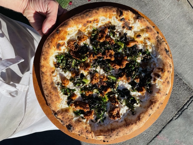 A pizza topped with pieces of Beyond sausage, kale and vegan cheese.